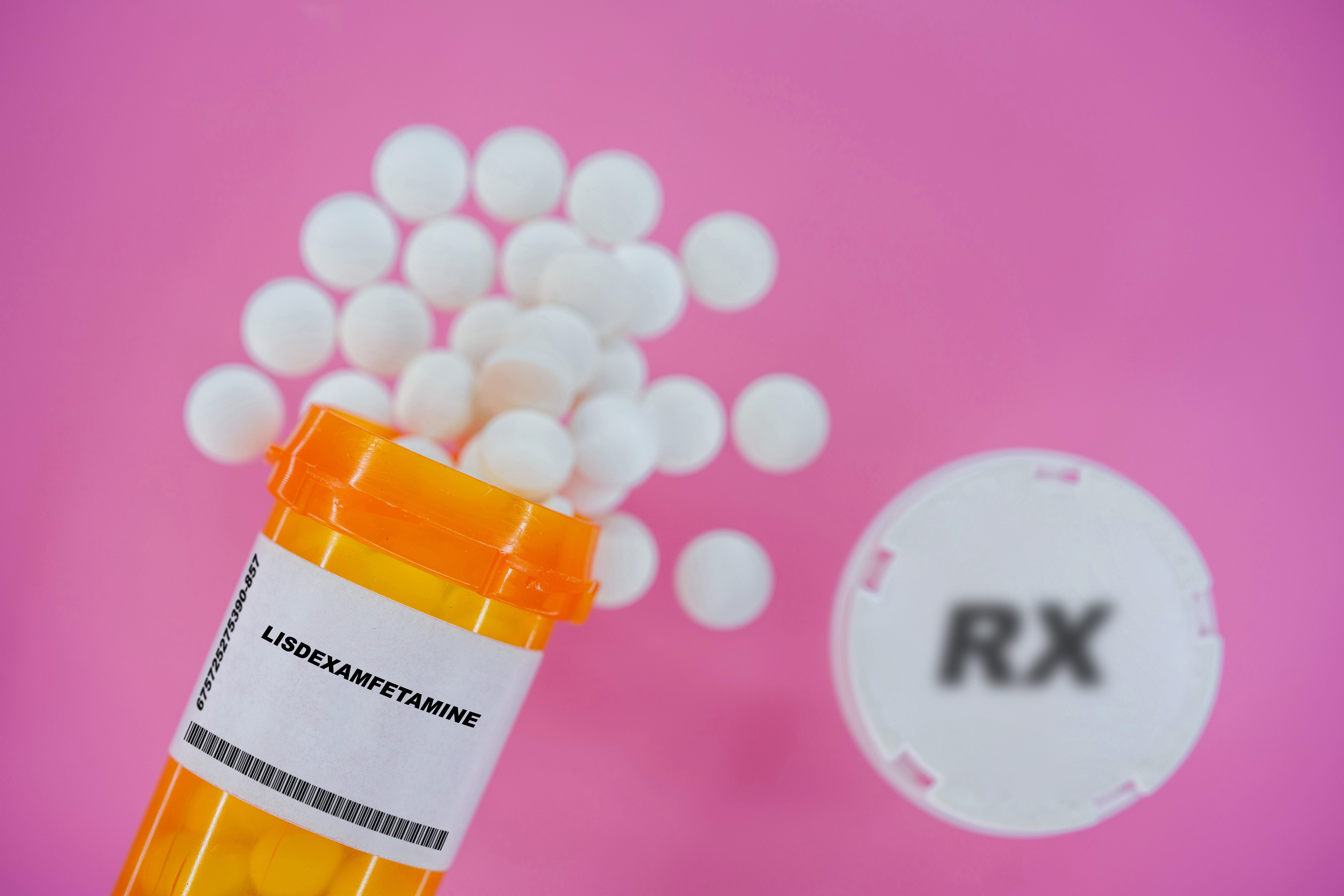Lisdexamfetamine Rx medicine pills in plactic vial with tablets. Pills spilling from yellow container on pink background. 